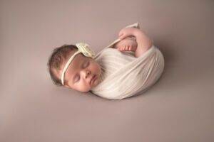 A newborn girl wrapped in a white blanket on a gray background.