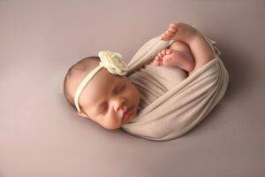 A newborn girl wrapped in a blanket on a beige background.