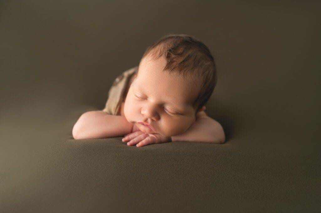A baby boy is laying down on a brown background.