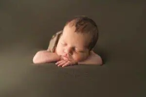 A baby boy is laying down on a brown background.