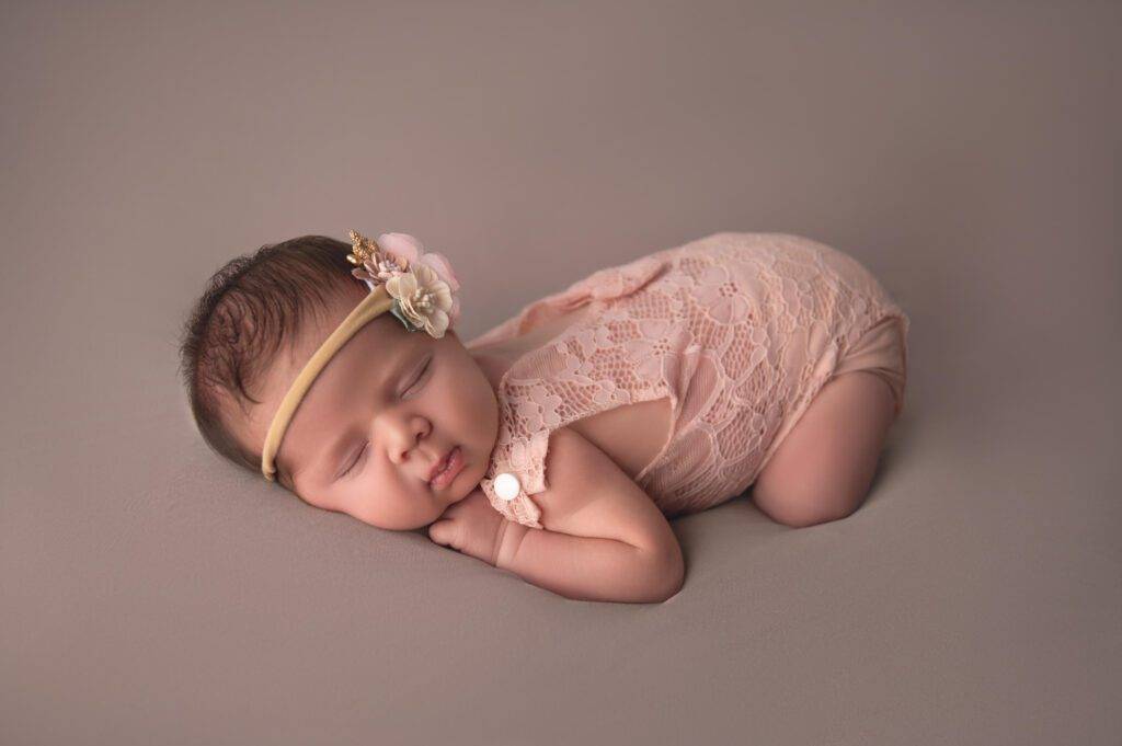 A baby girl in a pink outfit laying on a gray background.
