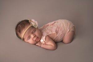 A baby girl in a pink outfit laying down on a gray background.