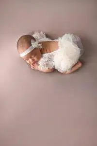 A baby girl in a white dress laying on a pink background.