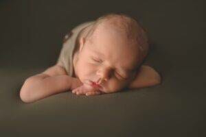 A newborn baby sleeping on a brown background.