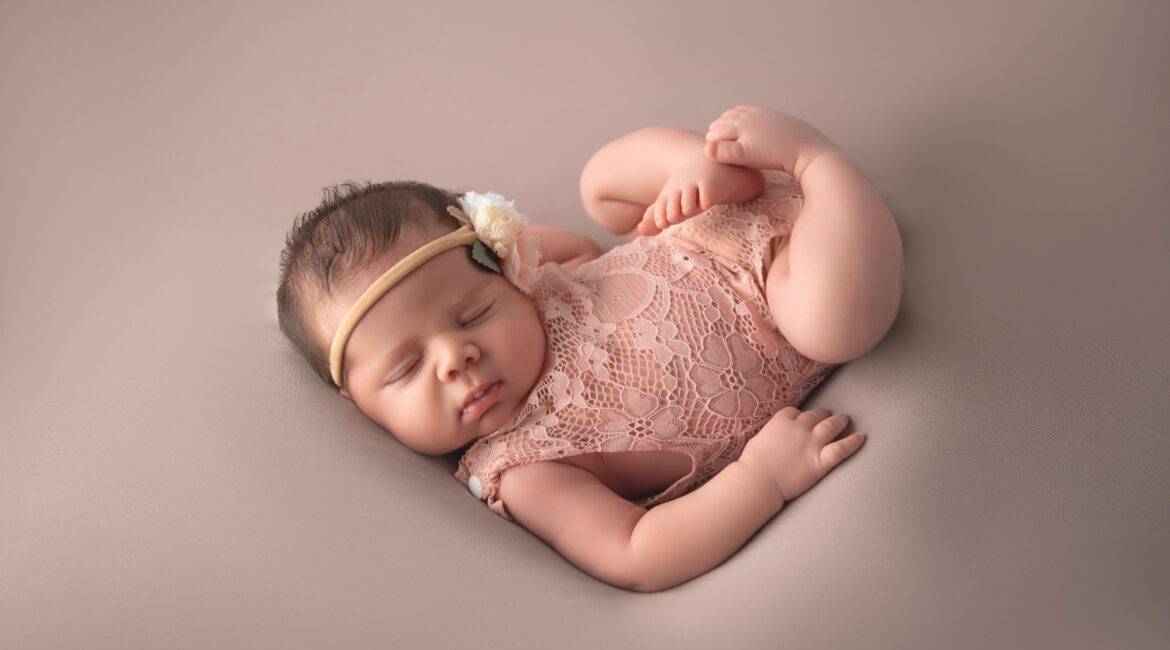 A newborn girl is laying down on a pink background.