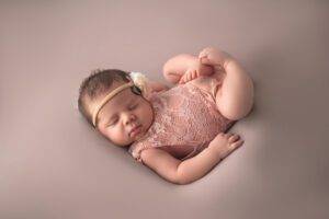 A newborn girl is laying down on a pink background.
