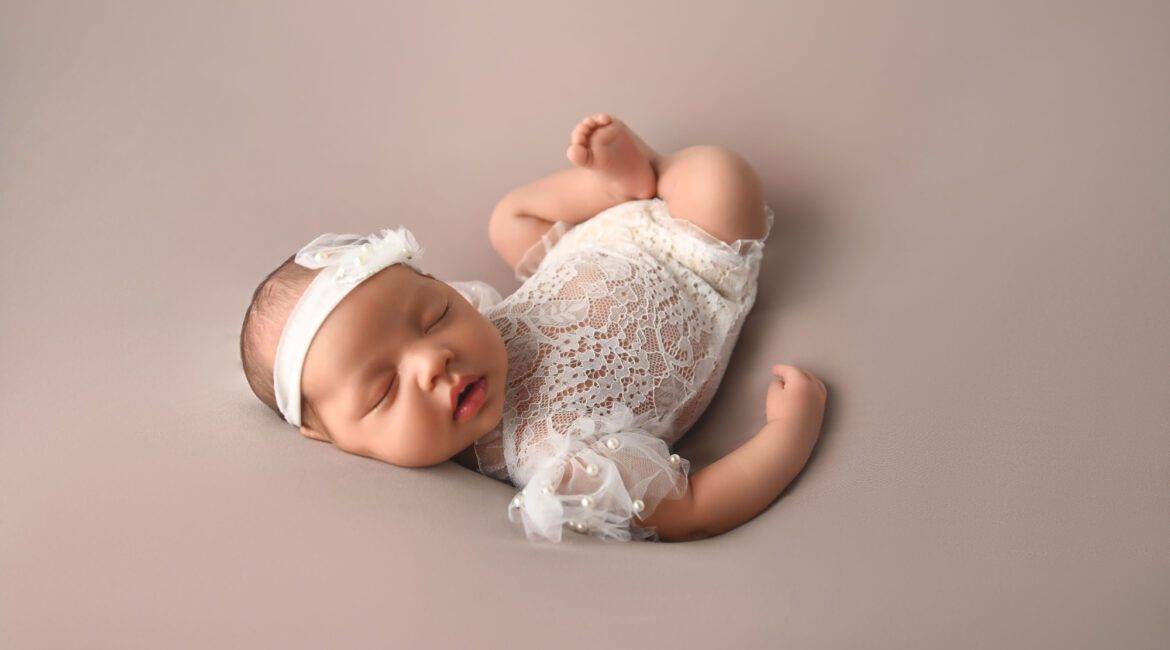 A newborn girl is laying on a grey background.