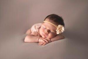 A baby girl laying on a grey background with a flower headband.