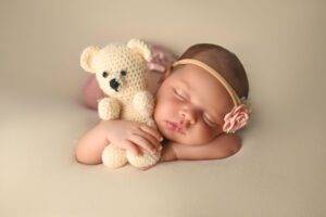 A baby sleeping with a crocheted teddy bear.