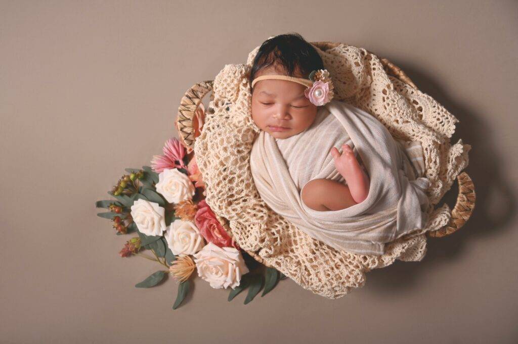 A baby girl is laying in a basket with flowers.