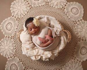 A newborn baby girl in a basket on a doily.