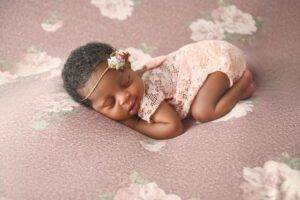 A baby girl is sleeping on a pink background.