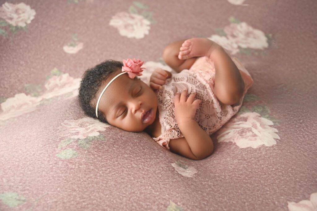A baby girl is laying on a pink floral background.