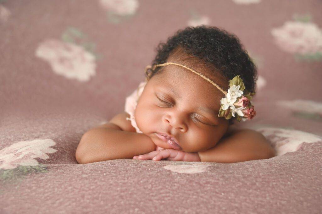 A baby girl sleeping on a pink floral blanket.