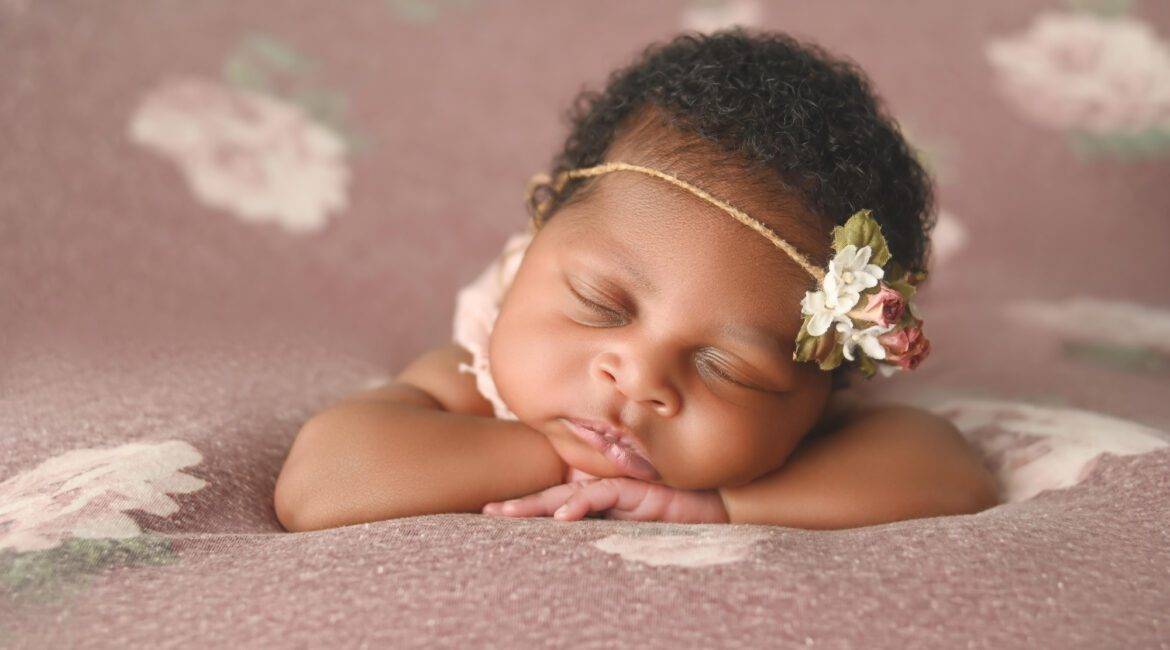 A baby girl sleeping on a pink floral blanket.