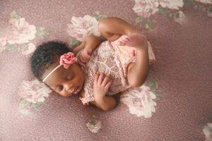 A baby girl is laying on a pink floral blanket.