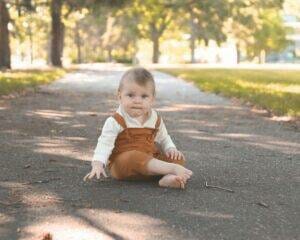 A baby sitting on a path in a park.