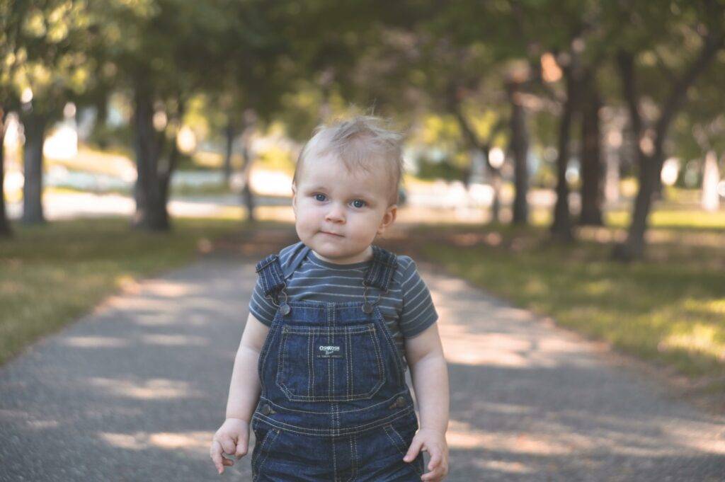 A baby boy in overalls standing on a path.