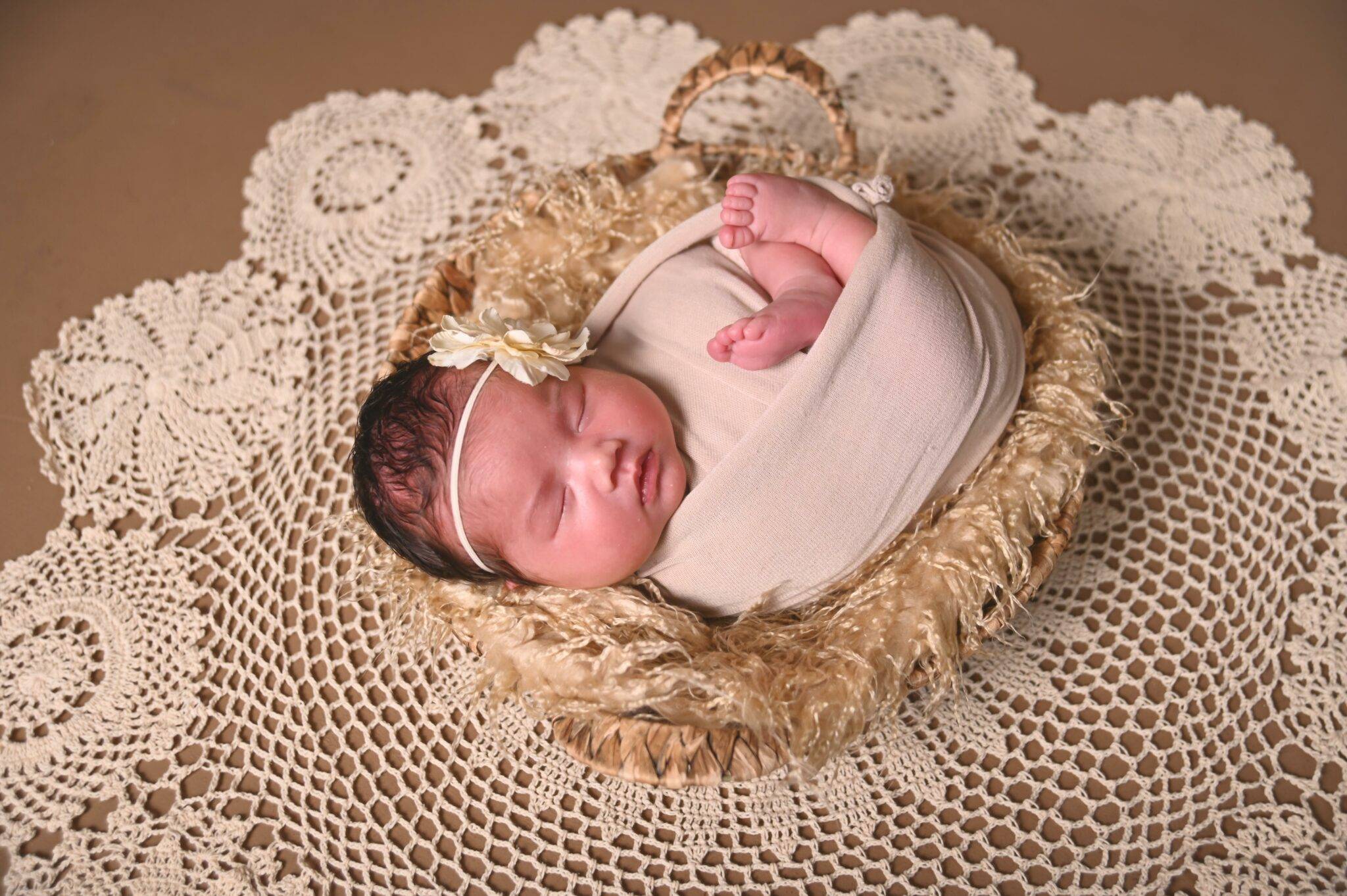A baby girl is laying in a basket on a doily.