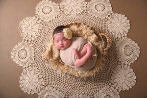 A baby girl is laying in a basket on a doily.