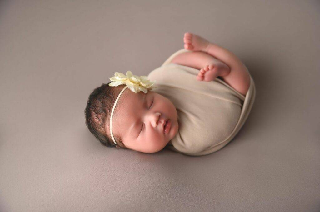 A baby girl wrapped in a blanket with a flower on her head.