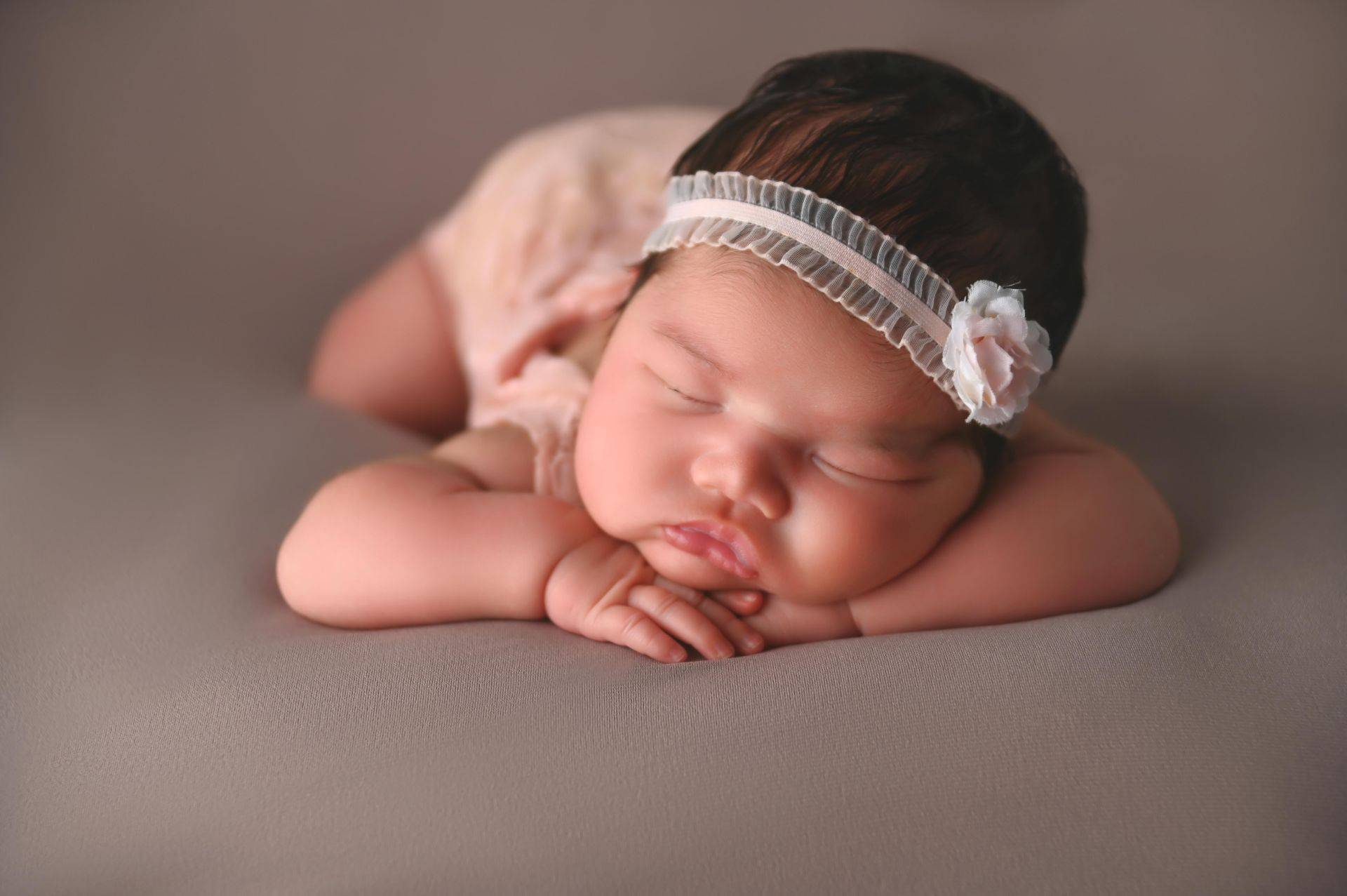 A baby girl is laying down on a gray background.