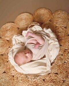 A baby is laying in a basket on a rug.