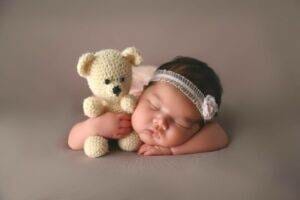 A baby sleeping with a crocheted teddy bear.