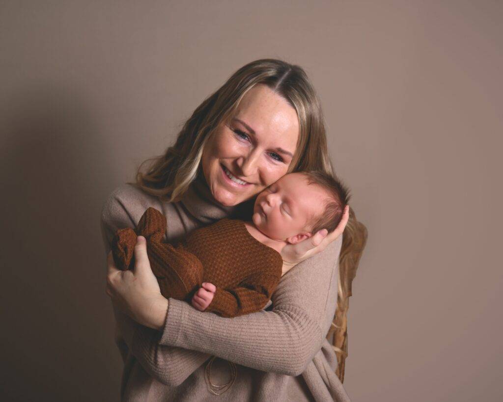 A woman holding a baby in a brown sweater.