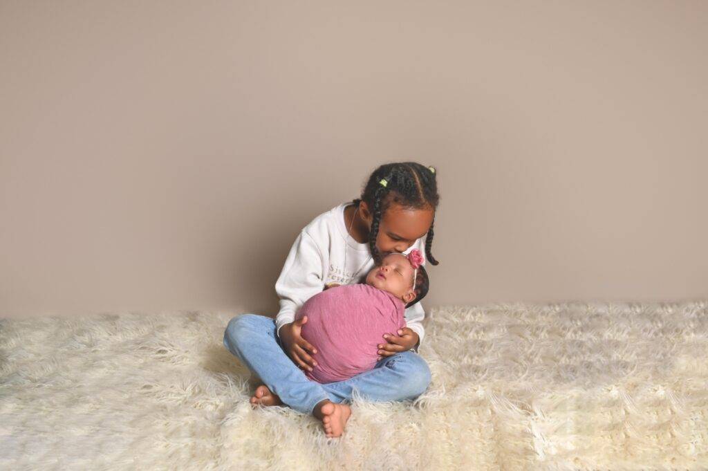 A woman is holding a baby on a white rug.