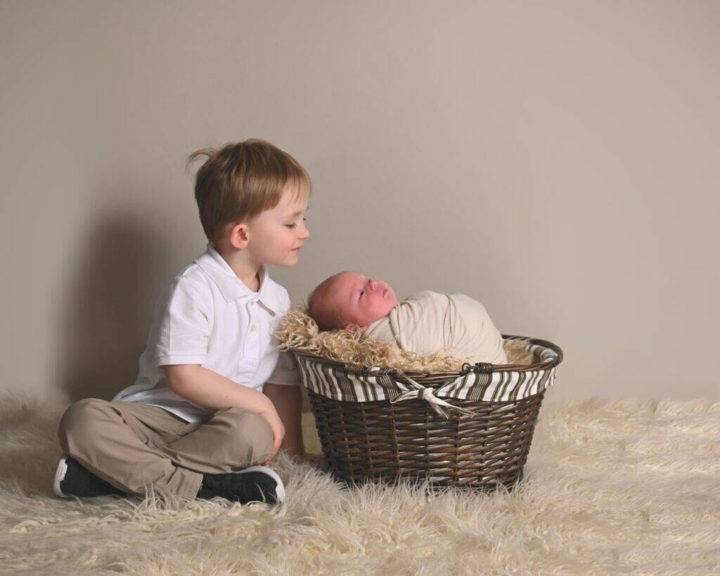 A boy sitting next to a baby in a basket.