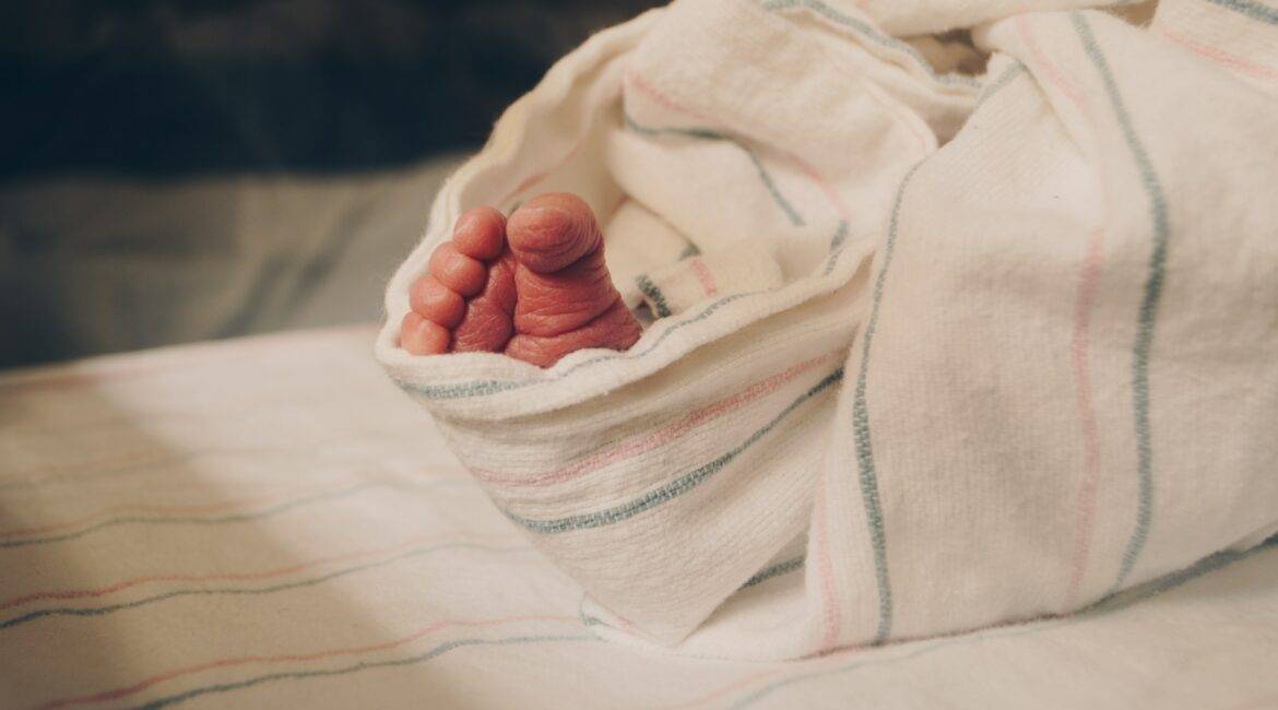 A baby's foot wrapped in a blanket on a bed.