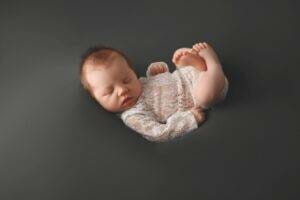 A newborn baby is resting on a grey background during a photoshoot in Saint Paul, Minnesota.