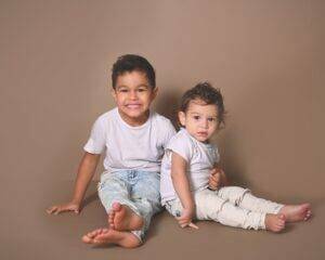 Two boys sitting on the floor in front of a brown background in a children photography session.