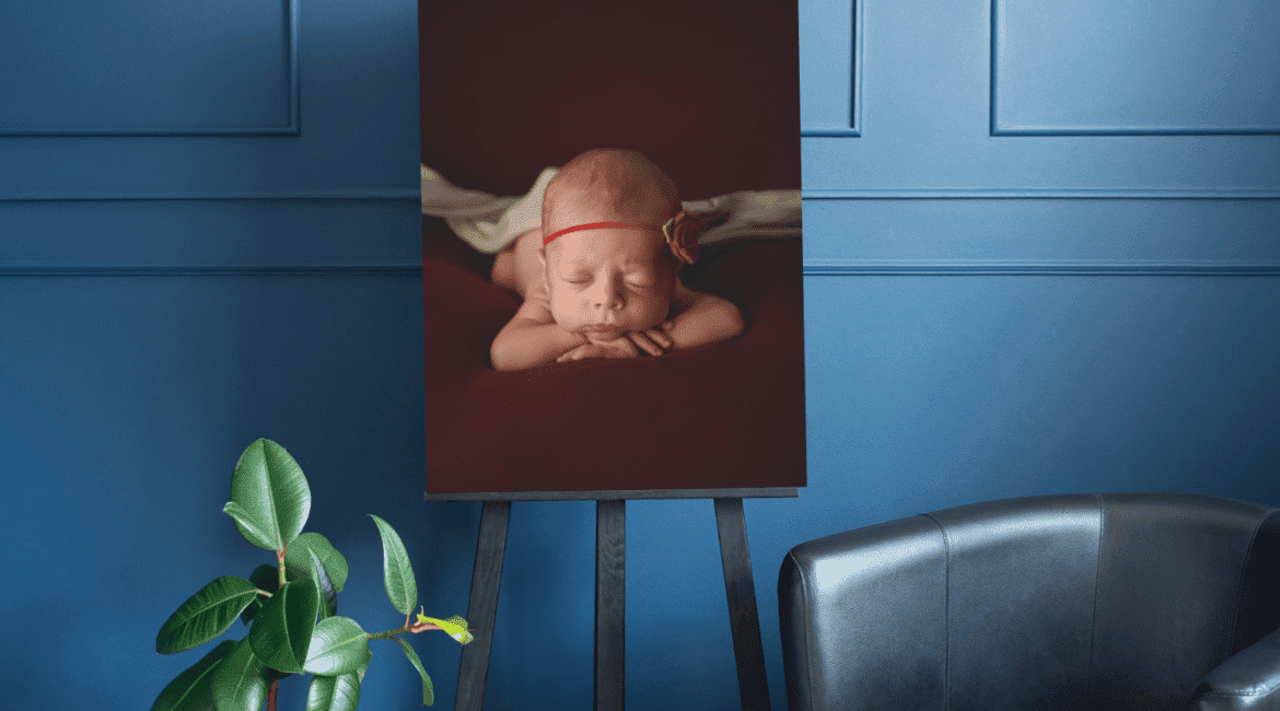 A photo of a baby lying on an easel in front of a blue wall.
