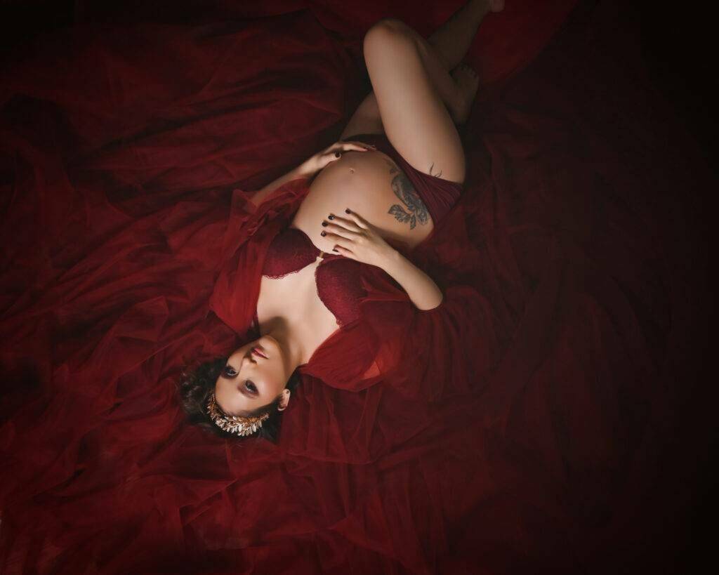 A pregnant woman lying on a red fabric.