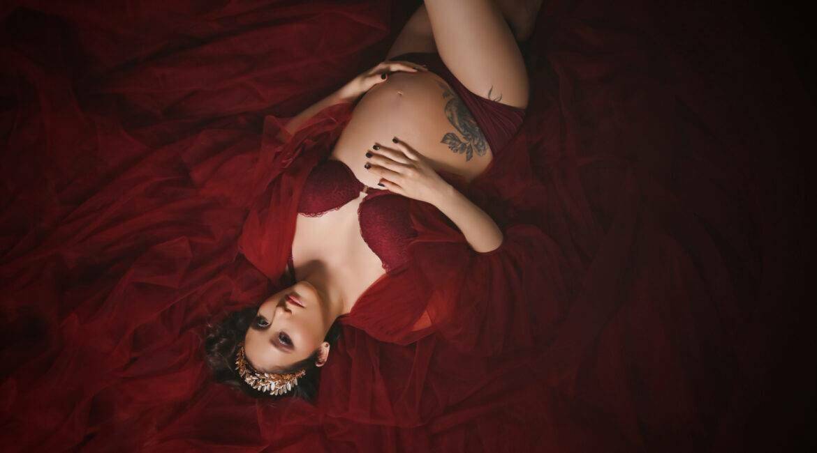A pregnant woman lying on a red fabric.