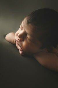 A newborn baby boy is laying on a dark background.