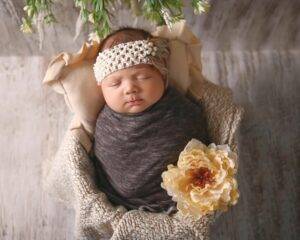 A baby girl is wrapped in a blanket and wearing a flower headband.