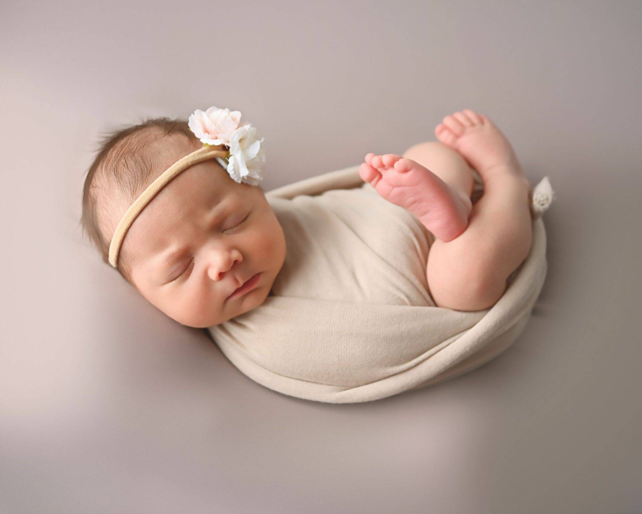 A newborn girl wrapped in a blanket with a flower on her head.