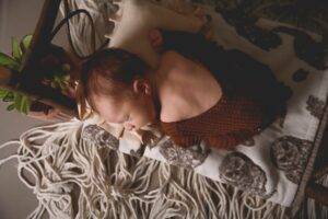 a newborn sleeping on a wooden bed with a patterned blanket with macrame floor. Saint paul minnesota