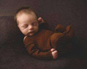 a newborn sleeping on a blanket on a brown surface.