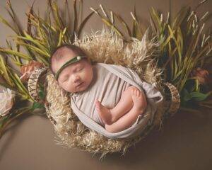 A baby girl is laying in a basket with grass and flowers.