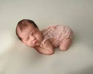 A baby girl in a pink outfit is laying on a white background.