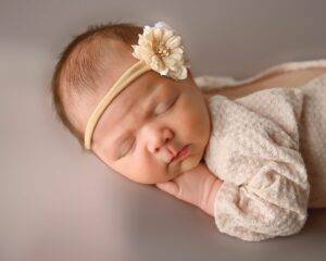 A baby girl sleeping with a flower headband on her head.