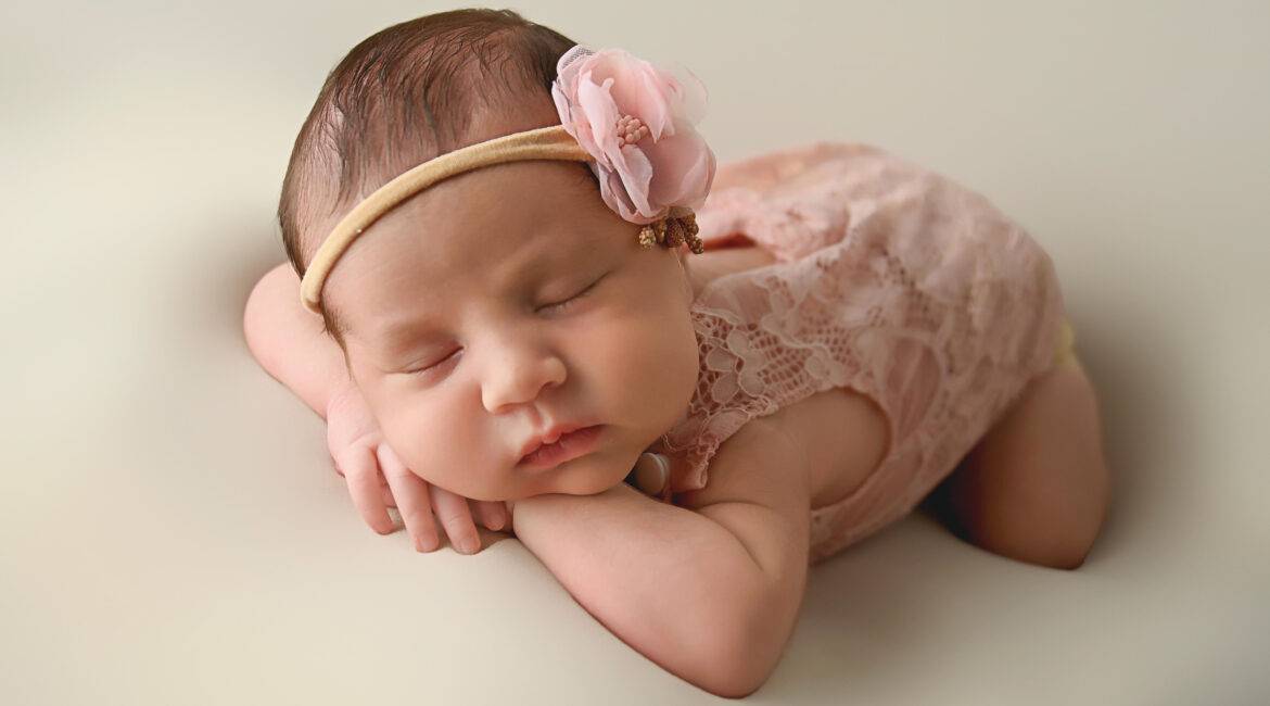 A baby girl is laying on a bed with a pink headband.