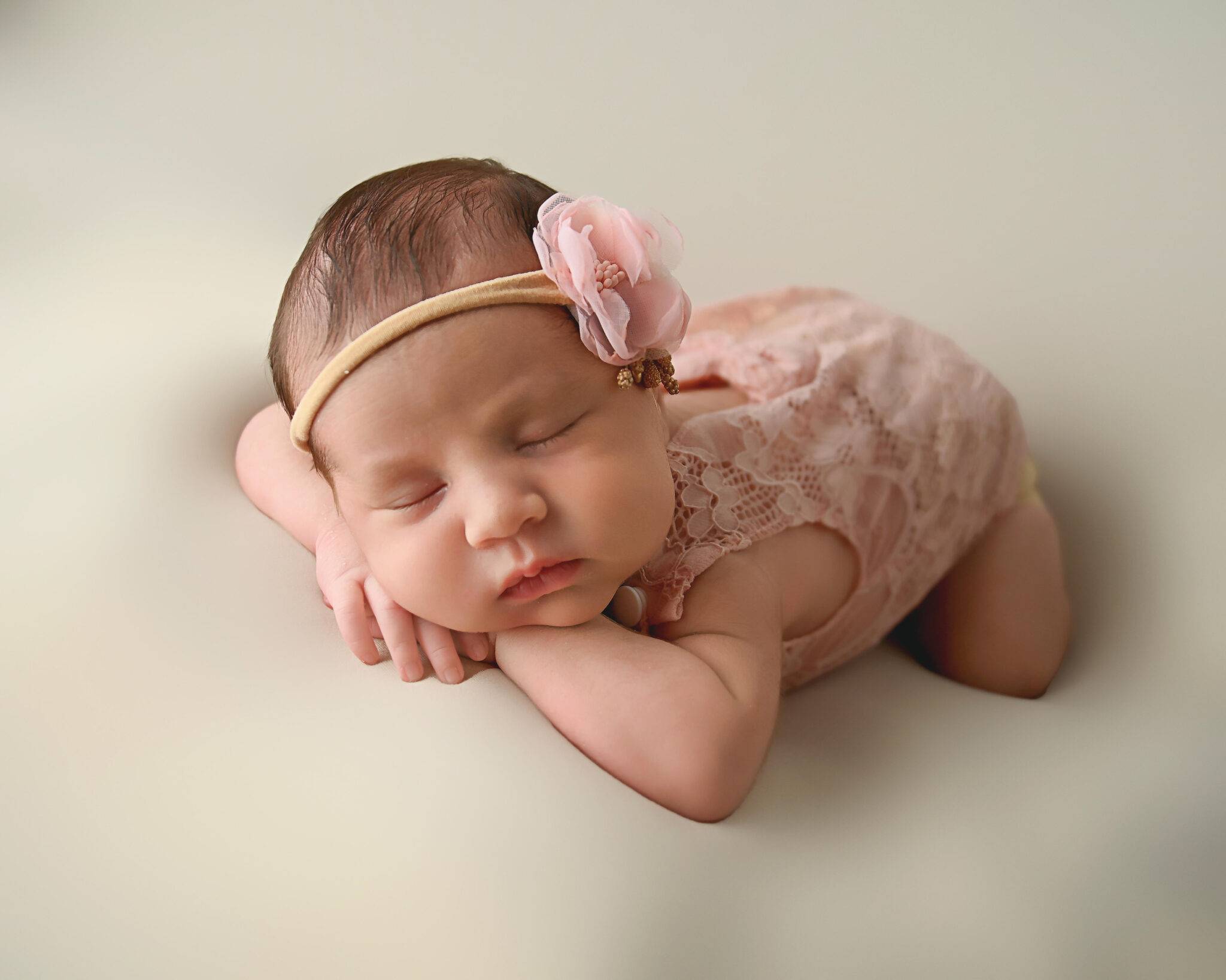 A baby girl is laying on a bed with a pink headband.