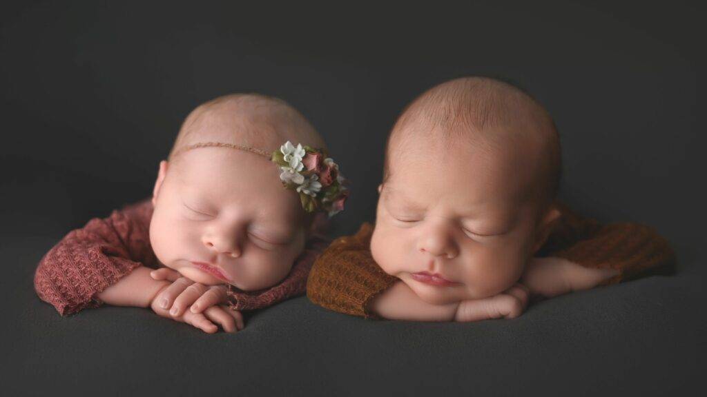 twin babies, with head on hands, asleep on grey background, posing for their newborn photography session