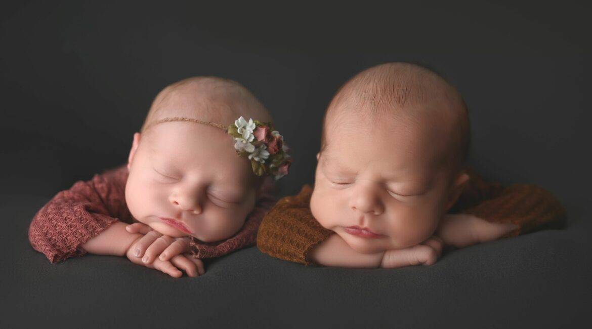 twin babies, with head on hands, asleep on grey background, posing for their newborn photography session