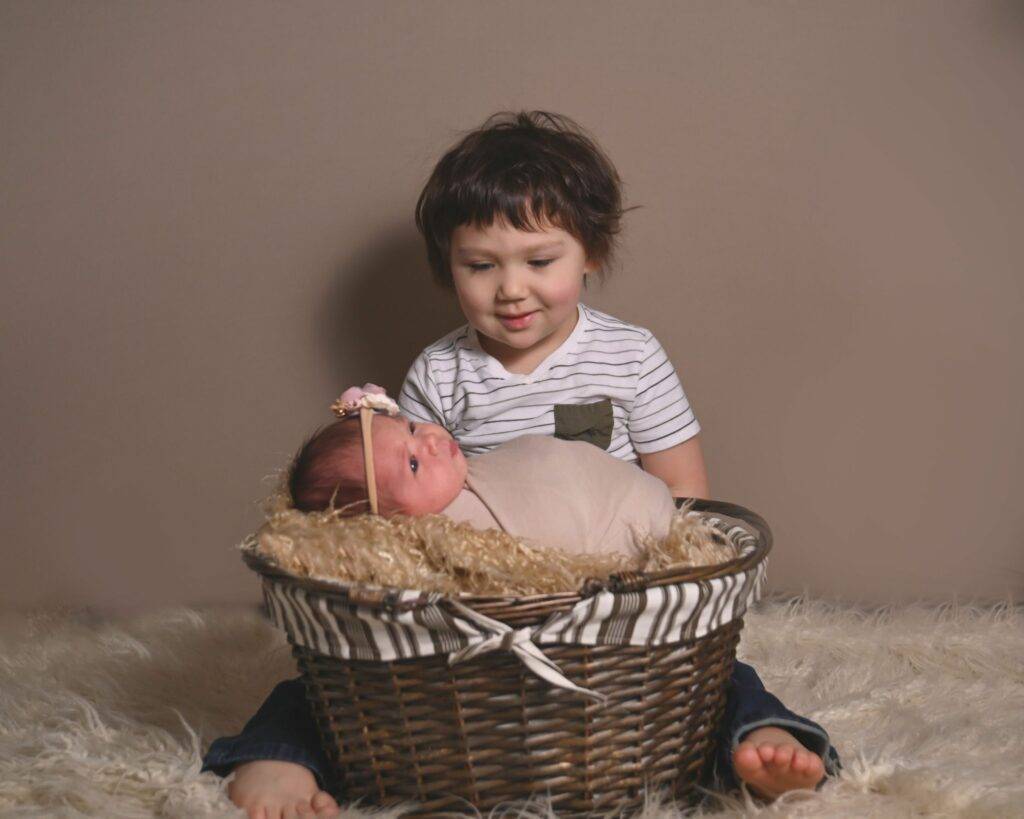 newborn in a basket and her big brother sitting next to her, looking at her